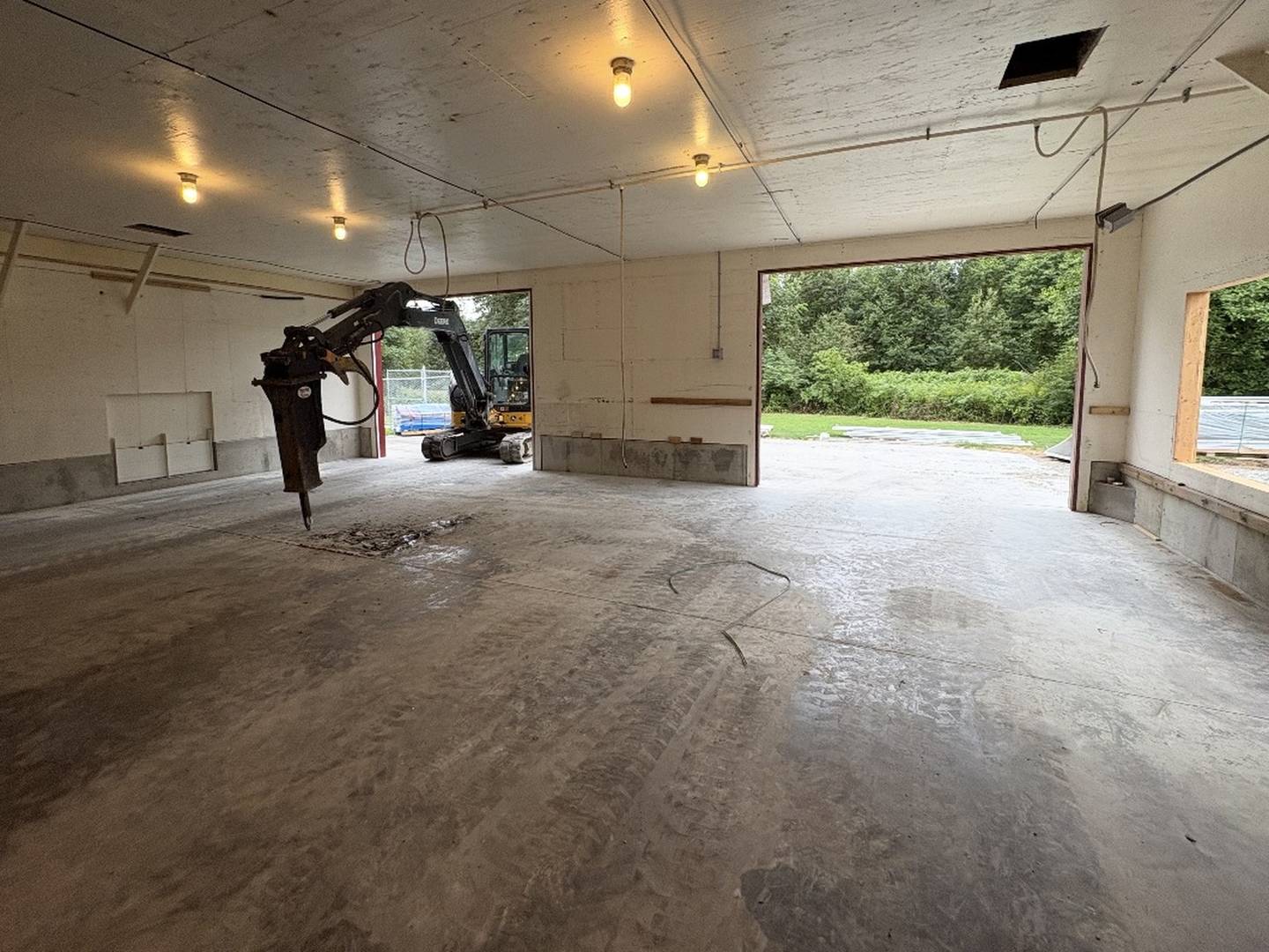 The bare concrete floor of a farm building with a compact excavator and hydraulic breaker standing inside