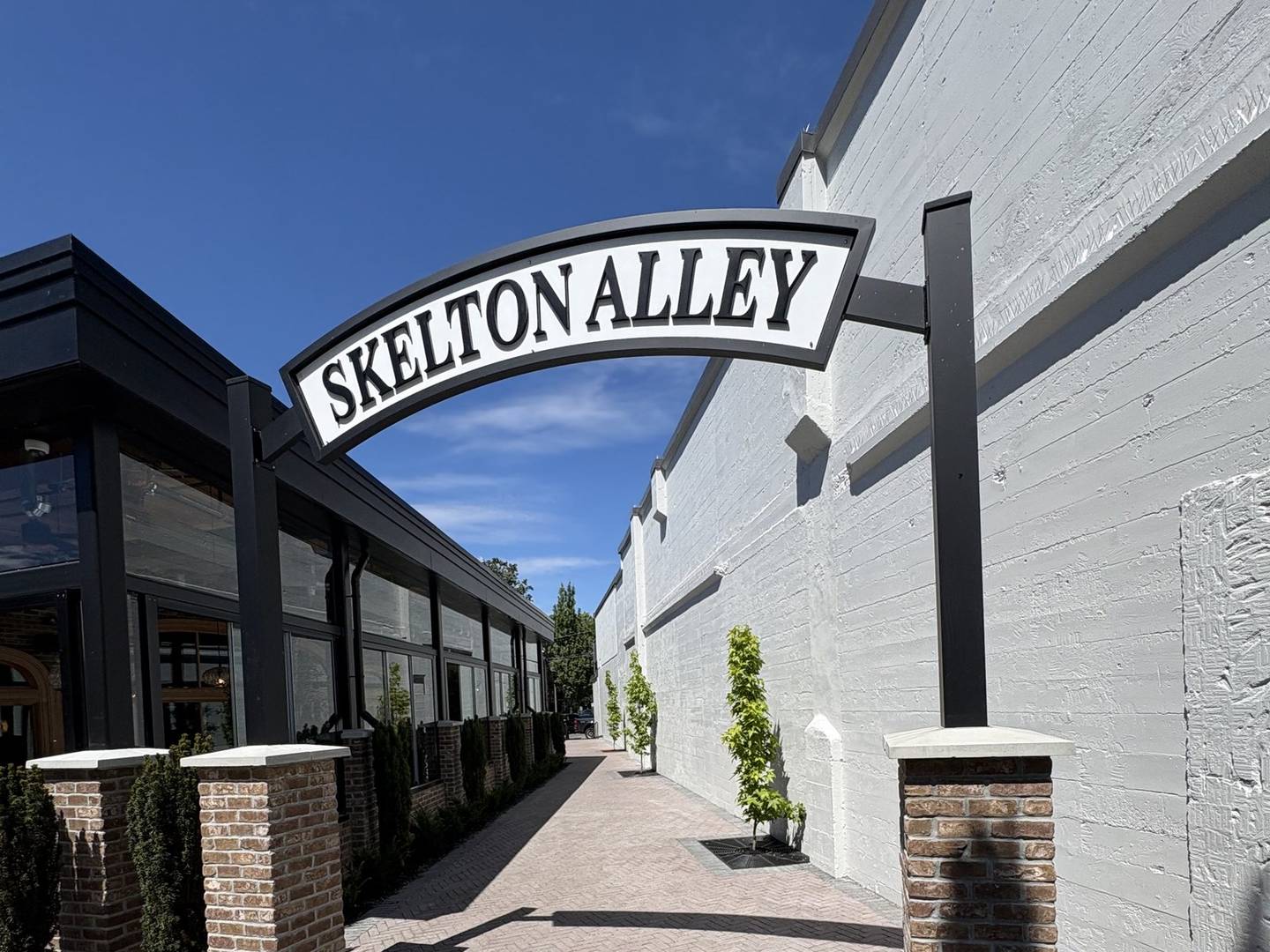 A herringbone brick paver walkway between two buildings, with brick pillars and a painted steel arch overhead