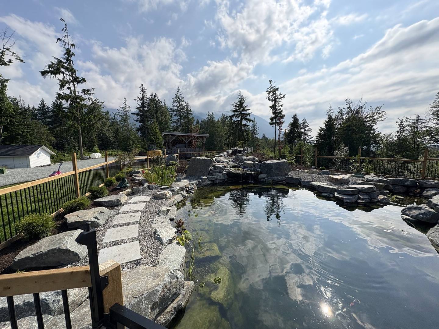 A landscaped pond edged with boulders, with a flagstone stepping-stone path, a waterfall inlet and mountains behind